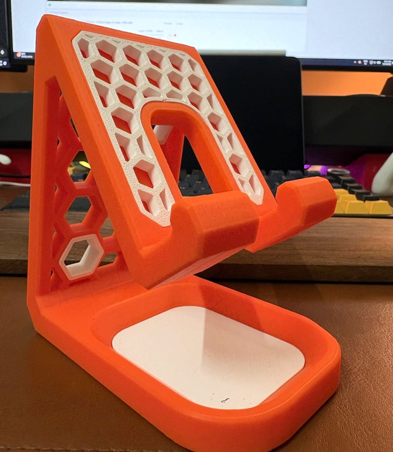 Orange and white honeycomb phone stand printed by DDPrinterZ, standing on a wooden desk