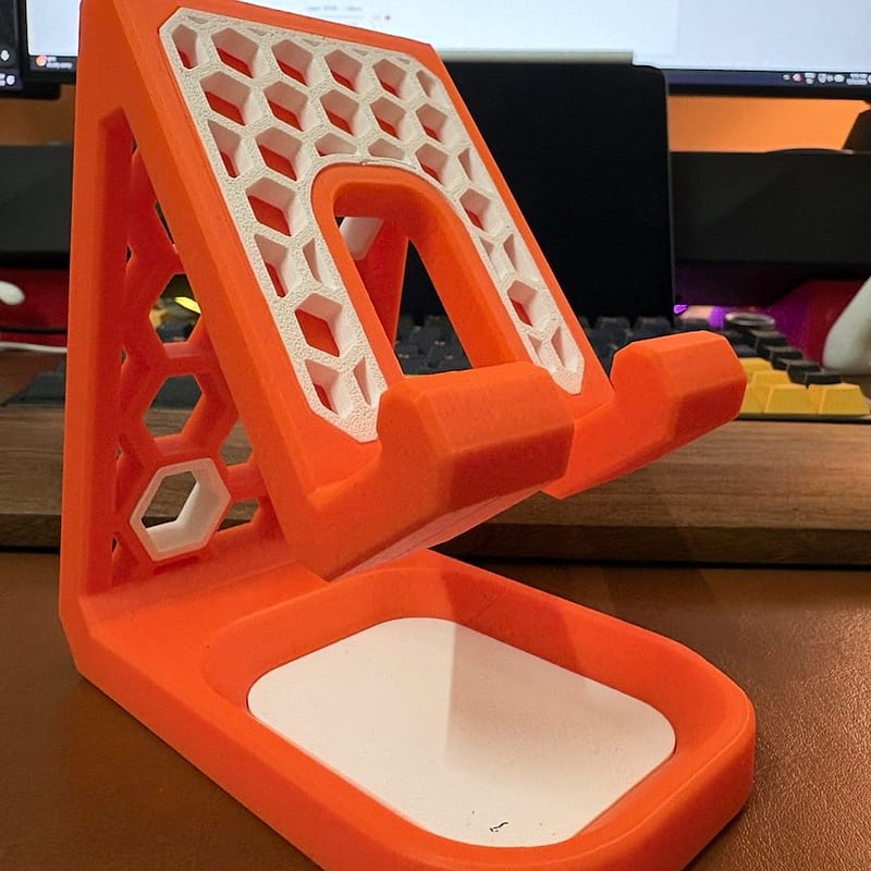 Orange and white honeycomb desk phone stand printed by DDPrinterZ, standing on a desk